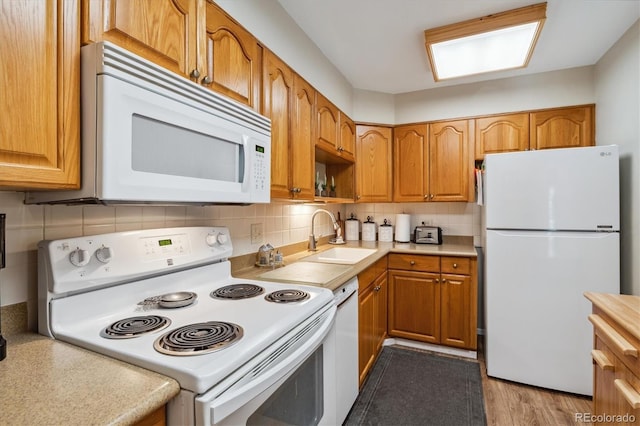 kitchen with decorative backsplash, white appliances, sink, and light hardwood / wood-style flooring