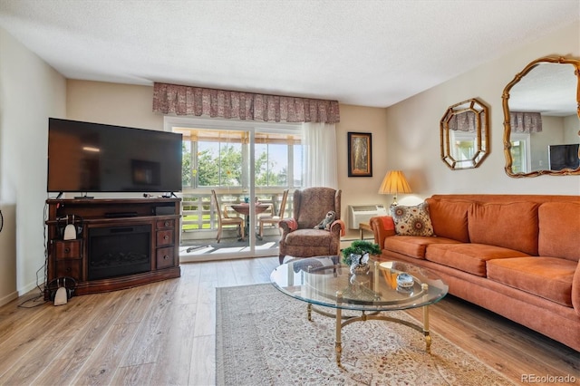 living room with light hardwood / wood-style floors, an AC wall unit, and a textured ceiling