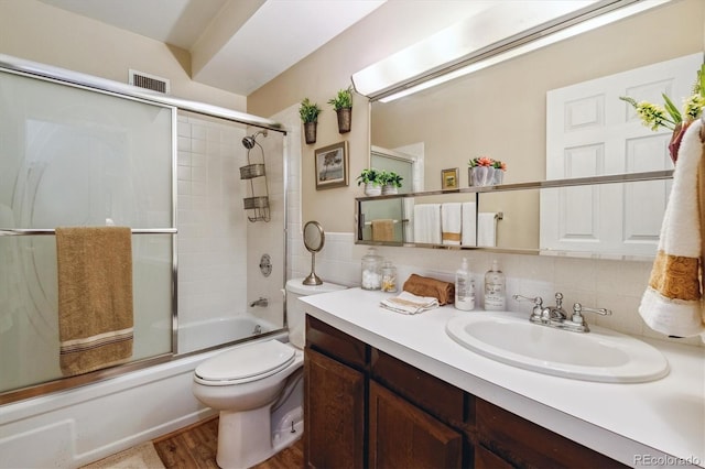 full bathroom with backsplash, bath / shower combo with glass door, wood-type flooring, toilet, and vanity