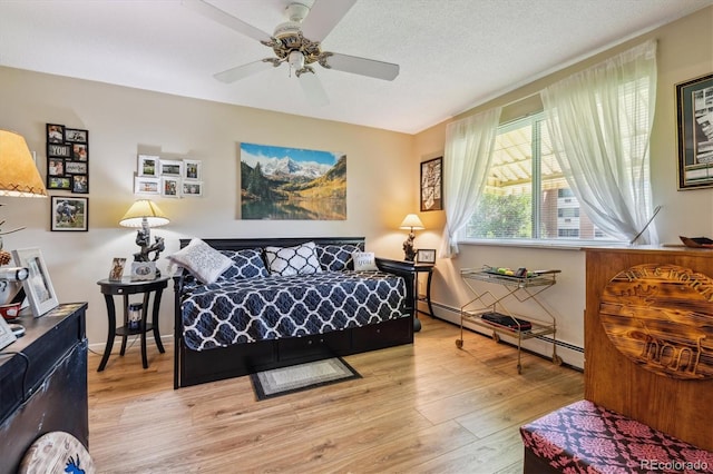 bedroom featuring ceiling fan, light hardwood / wood-style floors, a textured ceiling, and a baseboard heating unit