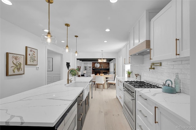 kitchen featuring pendant lighting, white cabinets, light stone countertops, an island with sink, and high end stove