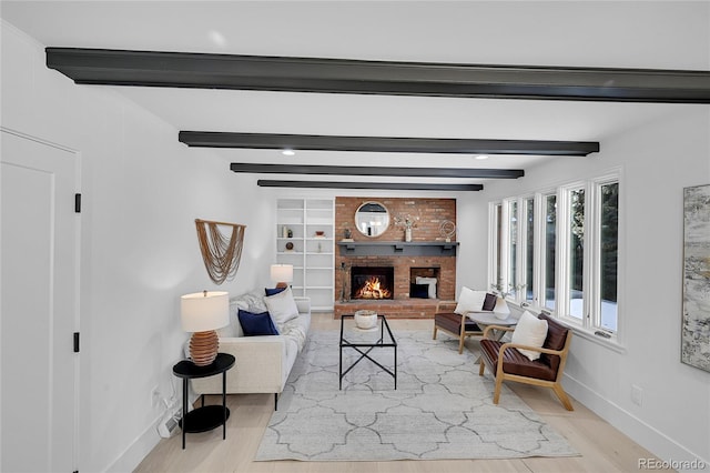 living room featuring built in shelves, light hardwood / wood-style flooring, beamed ceiling, and a brick fireplace