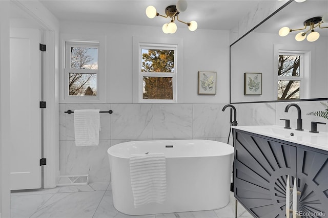 bathroom featuring a healthy amount of sunlight, a tub to relax in, vanity, and tile walls