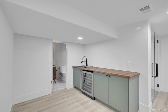 bar with wine cooler, sink, light wood-type flooring, green cabinetry, and wood counters