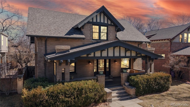 view of front of property with a porch, a shingled roof, and brick siding