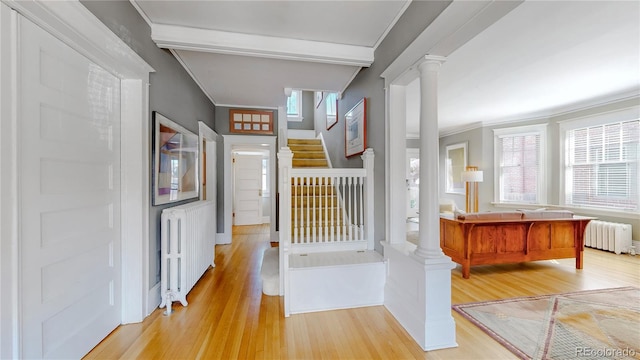 hallway with radiator, ornate columns, stairway, and light wood-style floors