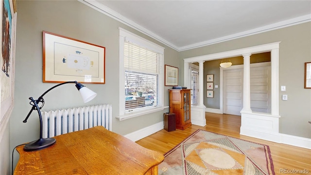 interior space featuring baseboards, radiator heating unit, light wood-style flooring, crown molding, and ornate columns