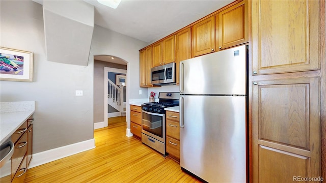 kitchen featuring light wood finished floors, baseboards, arched walkways, appliances with stainless steel finishes, and brown cabinets