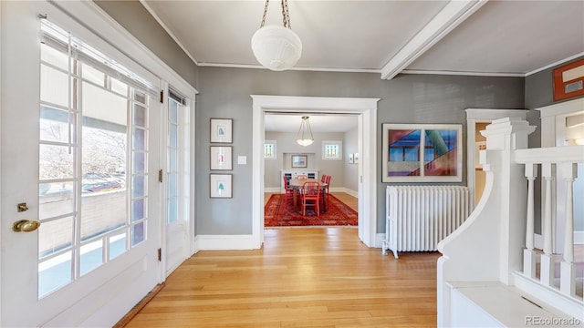 foyer entrance featuring light wood-type flooring, radiator, crown molding, and baseboards