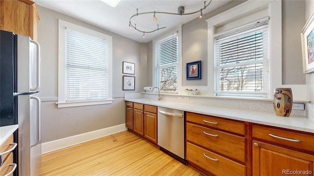 kitchen featuring brown cabinets, stainless steel appliances, light wood-style flooring, a sink, and baseboards