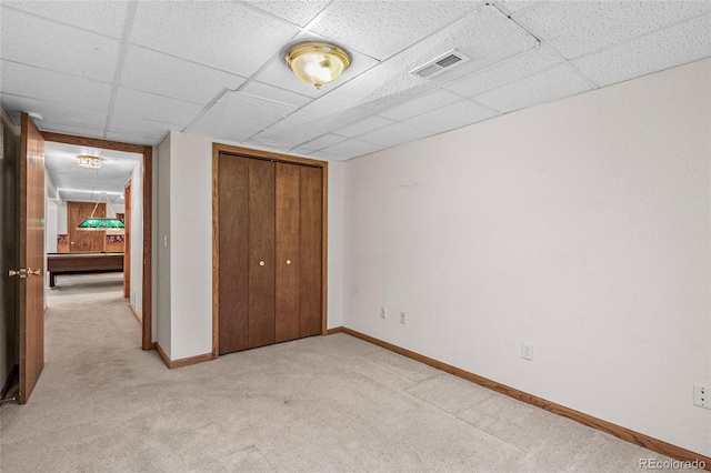 unfurnished bedroom with light carpet, a paneled ceiling, and a closet