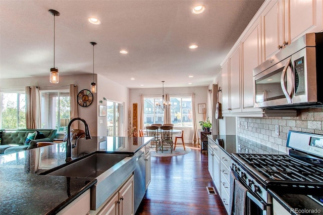 kitchen with an inviting chandelier, stainless steel appliances, sink, decorative light fixtures, and backsplash