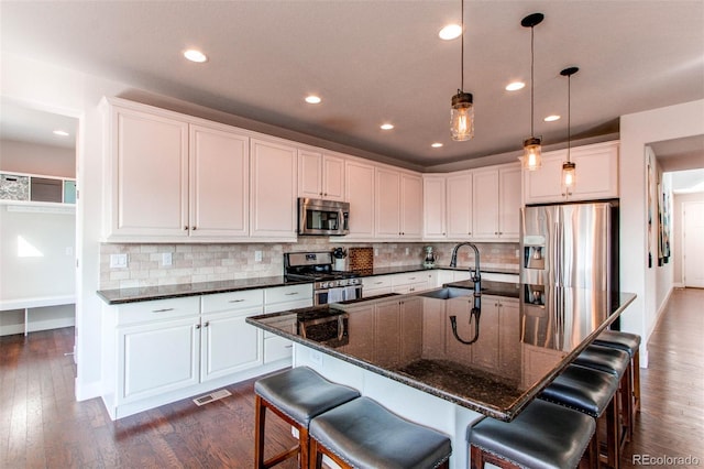 kitchen featuring stainless steel appliances, white cabinets, a kitchen bar, an island with sink, and pendant lighting