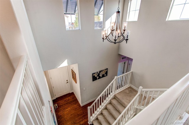 stairway with an inviting chandelier, a towering ceiling, and hardwood / wood-style flooring