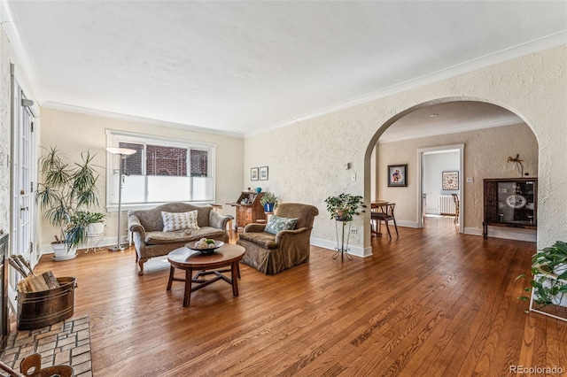 living room with crown molding, wood-type flooring, a textured wall, and baseboards