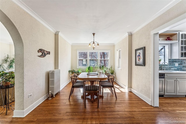 dining room with arched walkways, wood finished floors, baseboards, ornamental molding, and radiator