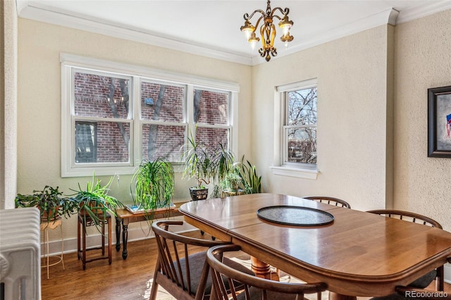 dining area with baseboards, a textured wall, wood finished floors, crown molding, and a chandelier