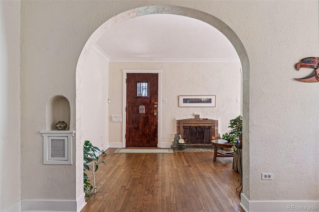 entrance foyer featuring arched walkways, wood-type flooring, a textured wall, ornamental molding, and baseboards