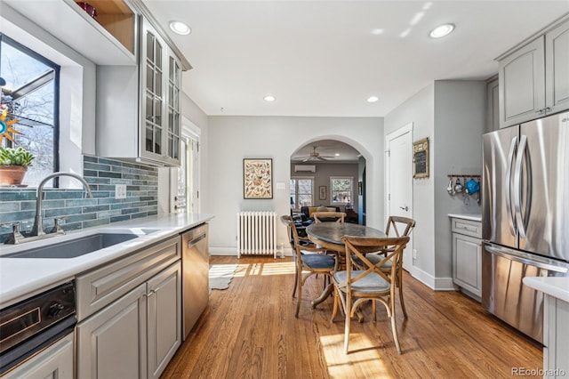 kitchen with arched walkways, radiator, appliances with stainless steel finishes, gray cabinetry, and a sink