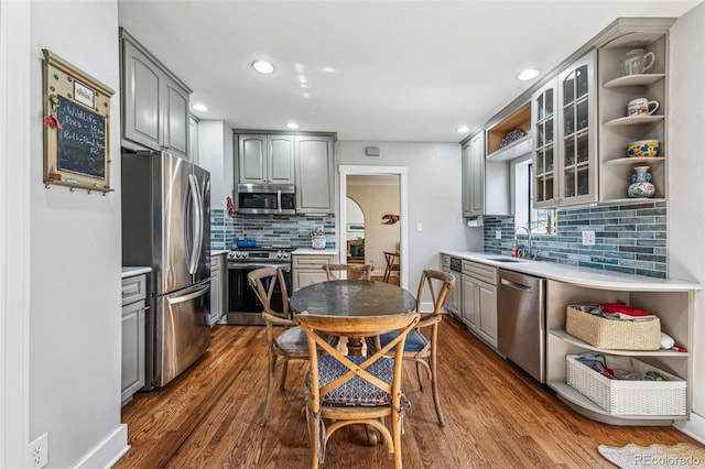 kitchen with dark wood finished floors, open shelves, stainless steel appliances, gray cabinets, and a sink