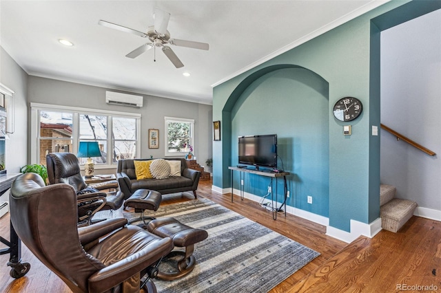 living area featuring a wall mounted AC, ornamental molding, wood finished floors, baseboards, and stairs