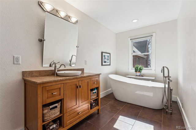 bathroom with a freestanding tub, tile patterned flooring, baseboards, and vanity