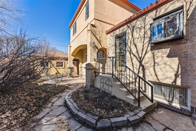 entrance to property with a tiled roof, a patio area, and stucco siding