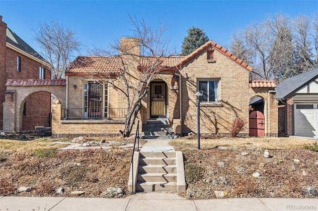 view of front of house featuring an attached garage, brick siding, a chimney, and a tiled roof