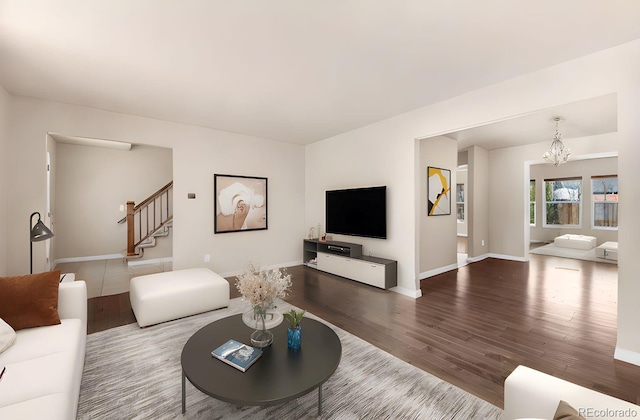 living area featuring stairway, baseboards, an inviting chandelier, and wood finished floors