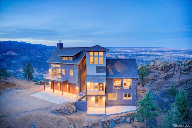 view of front of home featuring a patio, stone siding, a balcony, a chimney, and driveway