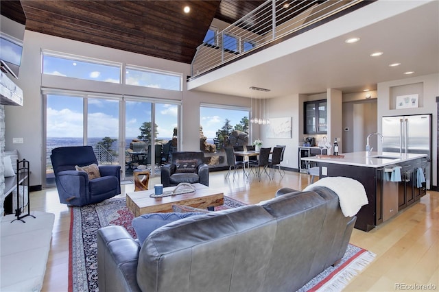 living area featuring a towering ceiling, baseboards, recessed lighting, light wood-style floors, and wood ceiling