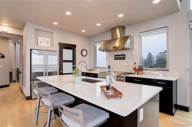 kitchen with wall chimney exhaust hood, a healthy amount of sunlight, a sink, stainless steel appliances, and dark cabinetry