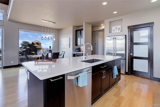 kitchen featuring a sink, light countertops, light wood-type flooring, appliances with stainless steel finishes, and an island with sink