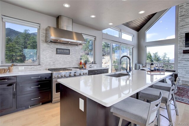 kitchen featuring wall chimney exhaust hood, tasteful backsplash, stainless steel stove, light countertops, and light wood finished floors
