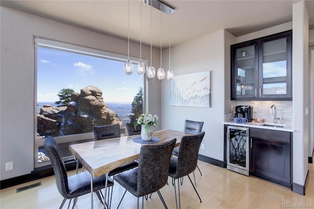 dining area with visible vents, baseboards, indoor wet bar, wine cooler, and light wood-style flooring