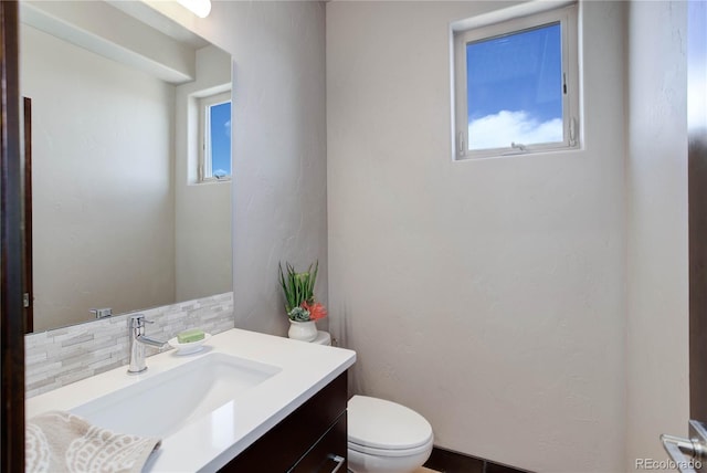 half bathroom featuring a wealth of natural light, vanity, backsplash, and toilet