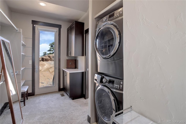 laundry room with a textured wall, light colored carpet, stacked washing maching and dryer, and laundry area