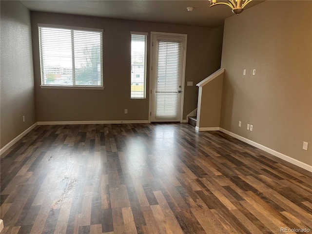 unfurnished living room with stairway, baseboards, dark wood-style flooring, and a chandelier