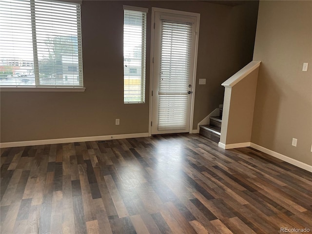 unfurnished room featuring a healthy amount of sunlight, baseboards, stairway, and dark wood-type flooring