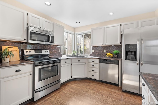 kitchen featuring appliances with stainless steel finishes, a sink, light wood-style floors, white cabinetry, and recessed lighting