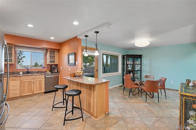 kitchen with a kitchen breakfast bar, hanging light fixtures, light brown cabinetry, stainless steel dishwasher, and sink