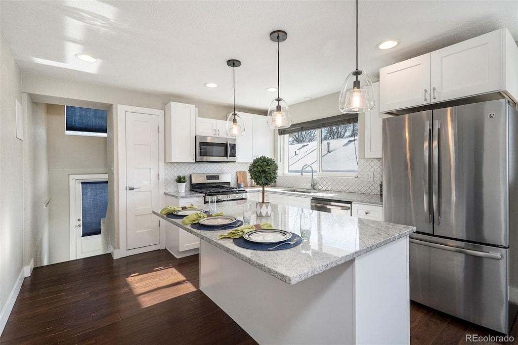 kitchen with sink, white cabinets, light stone countertops, a kitchen island, and stainless steel appliances