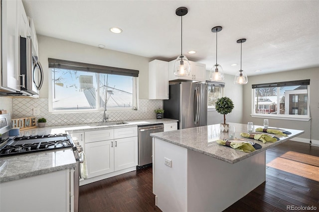 kitchen with a kitchen island, light stone counters, white cabinets, and appliances with stainless steel finishes