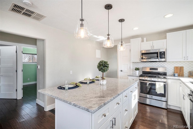 kitchen featuring white cabinets, a center island, decorative light fixtures, stainless steel appliances, and decorative backsplash