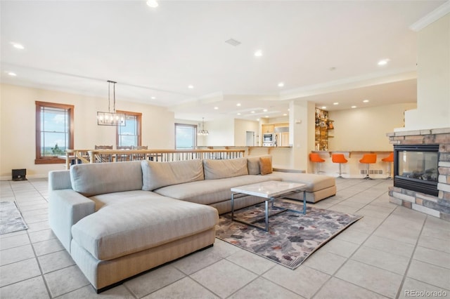 tiled living room featuring crown molding, plenty of natural light, a chandelier, and a stone fireplace