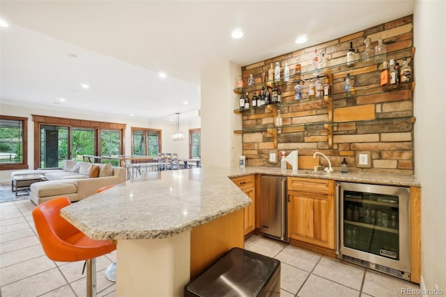 bar with light tile patterned floors, decorative light fixtures, light stone counters, sink, and beverage cooler