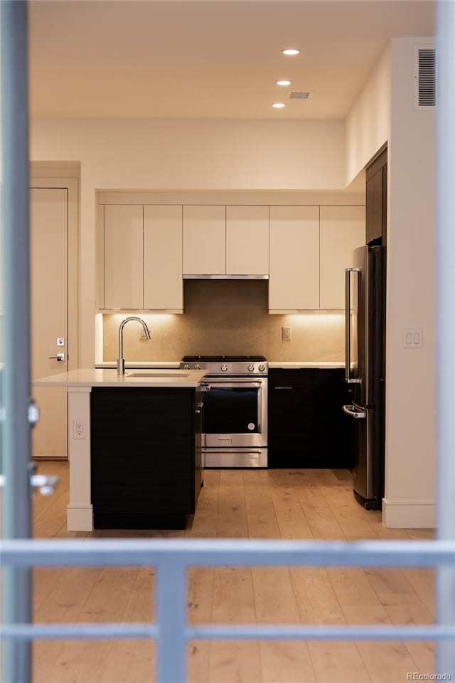 kitchen with sink, stainless steel gas range, high end fridge, tasteful backsplash, and white cabinets