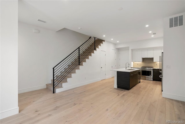 kitchen with sink, white cabinetry, light wood-type flooring, an island with sink, and high end stainless steel range oven