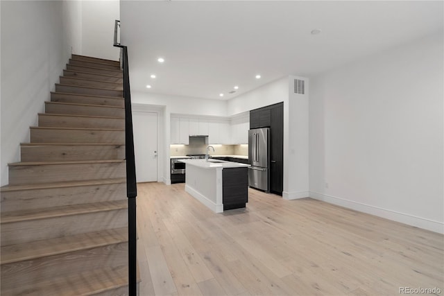 kitchen with sink, light hardwood / wood-style flooring, a kitchen island with sink, white cabinetry, and high end refrigerator