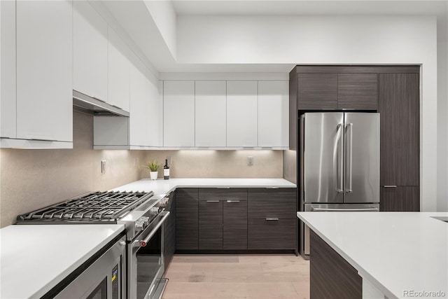 kitchen with under cabinet range hood, white cabinetry, dark brown cabinetry, light countertops, and high end appliances